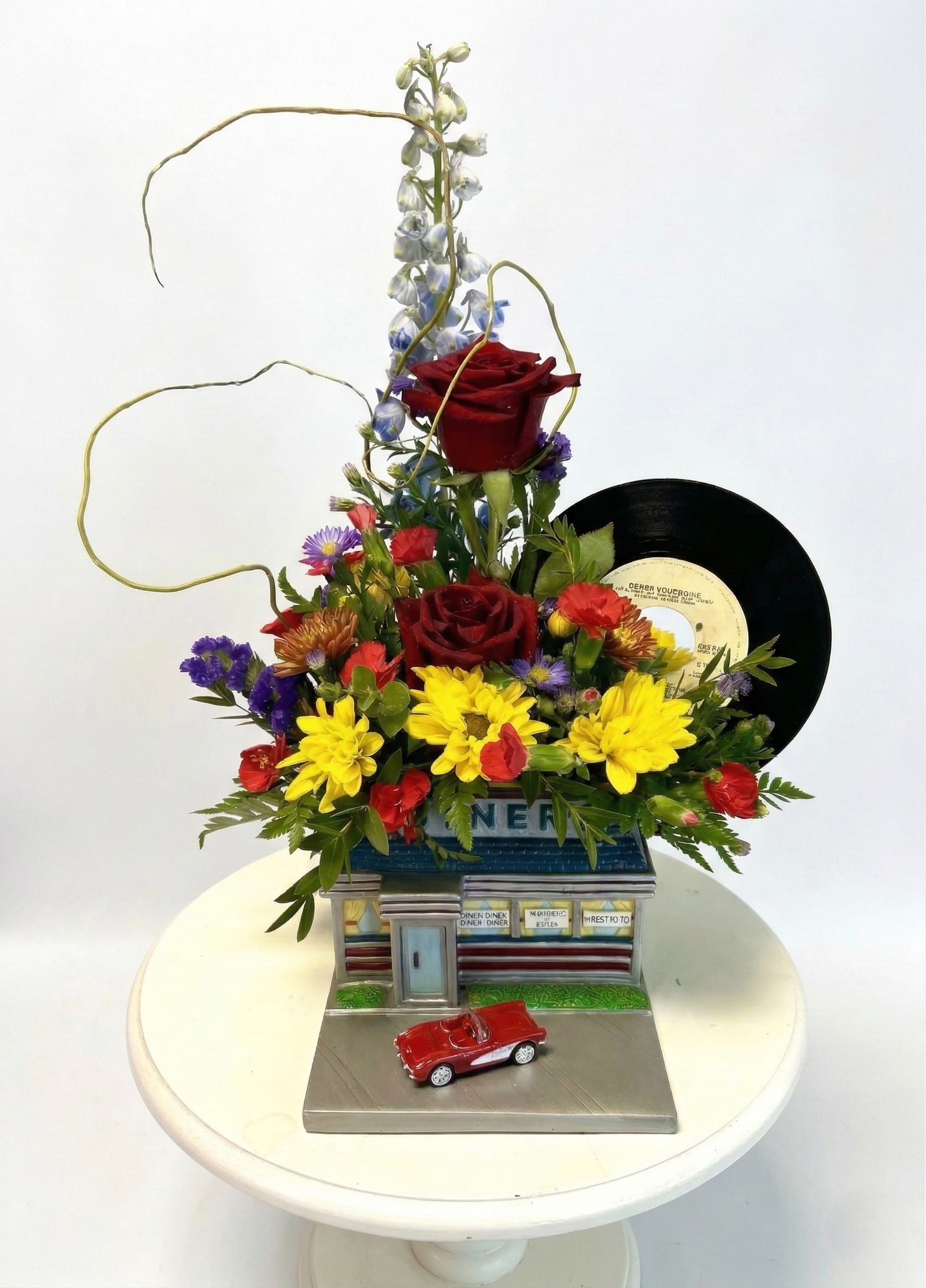 Mixed flower arrangement with roses, daisies, and a vinyl record on a decorative base