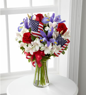 Bouquet of red roses and purple flowers with small American flags in a glass vase
