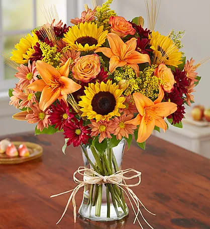 Bouquet of sunflowers, orange lilies, and roses in a clear glass vase