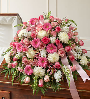 Large pink and white floral casket spray with ribbon on a wooden casket