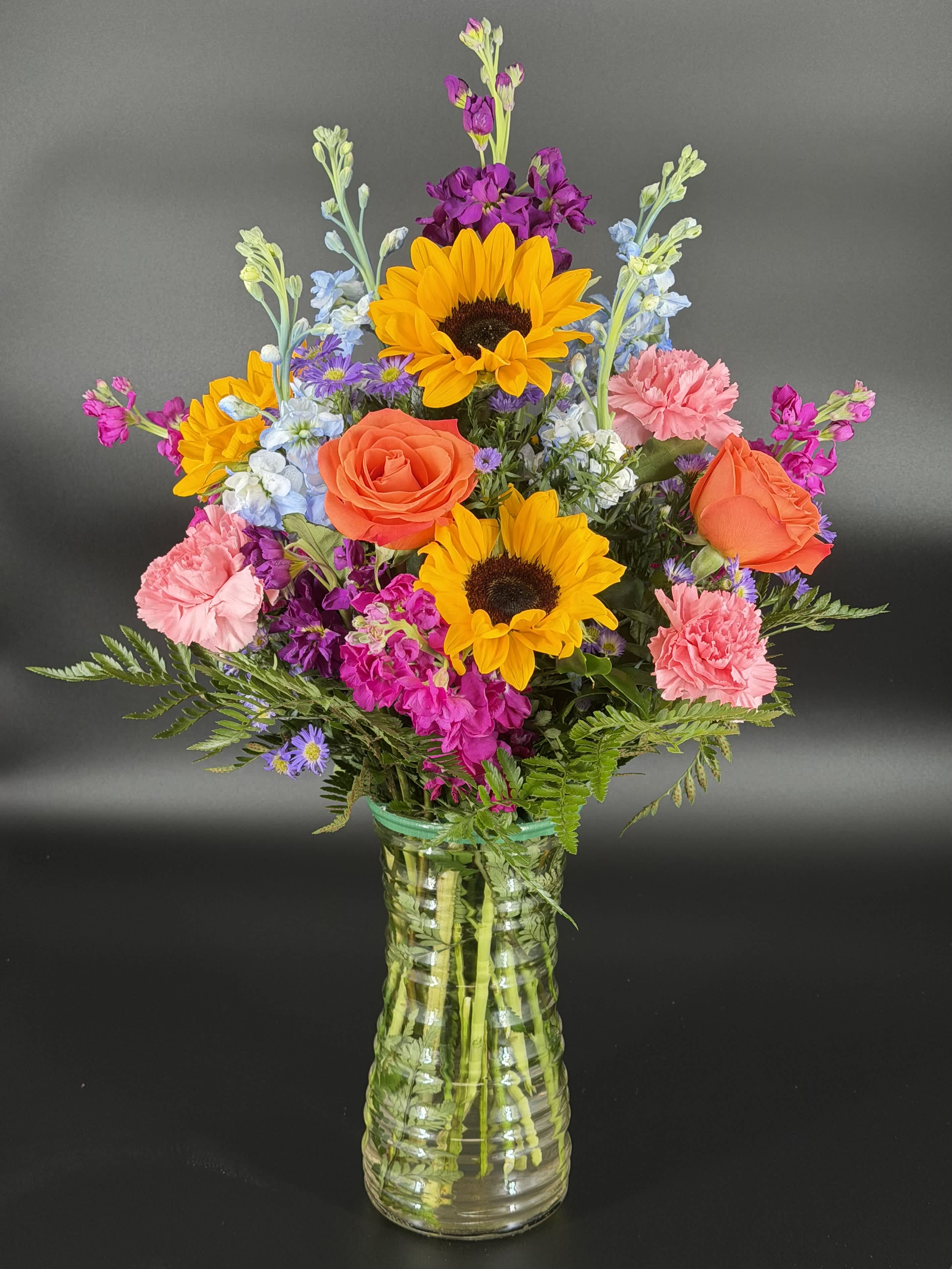 Colorful mixed bouquet in a clear glass vase with sunflowers, roses, and carnations
