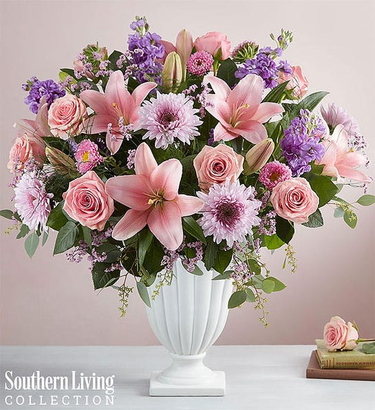 Pink lilies, roses, and purple flowers arranged in a white vase