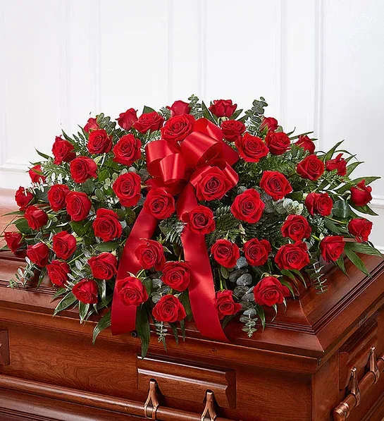 Red rose casket spray with a large red ribbon on a wooden casket