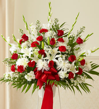 Tall red and white standing floral arrangement with roses, lilies, and bow on an easel