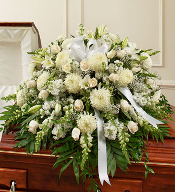 White funeral spray with lilies, roses, and ribbon on a casket
