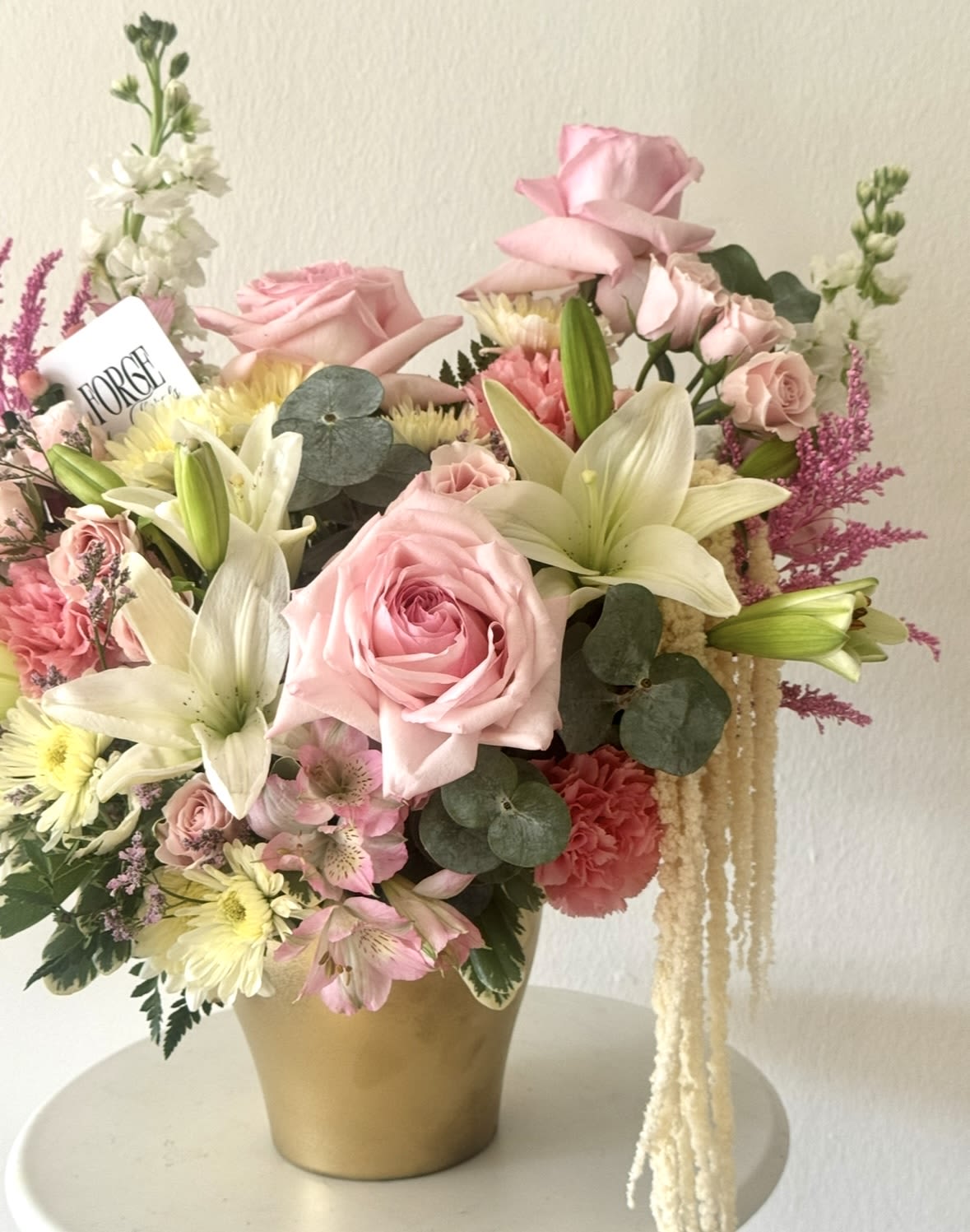 Love Letter arrangement- Lilly, Garden roses,Alstromeria, Stock - A lush garden-inspired arrangement featuring soft pink roses, delicate spray roses, elegant white lilies, airy astilbe, and seasonal blooms gathered in a golden keepsake vase. Designed with movement, texture, and a romantic wildflower feel, this piece brings together timeless elegance and playful charm. Perfect for birthdays, anniversaries, new beginnings, or simply making someone feel loved.