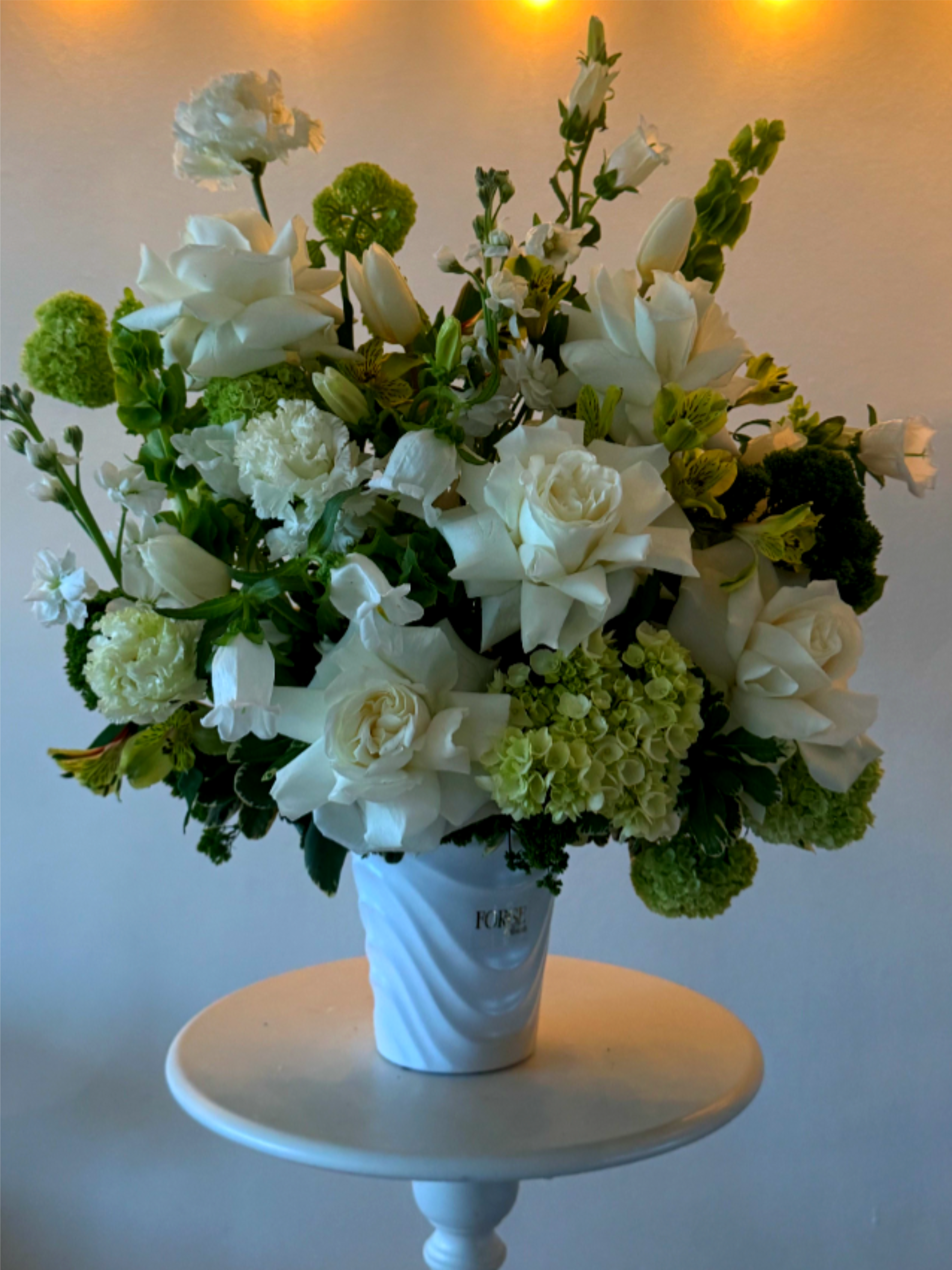 White floral arrangement in a white vase with green accents