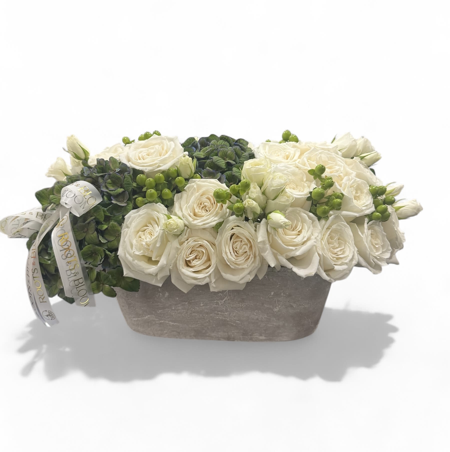 White roses arranged in a low rectangular vase with green berries