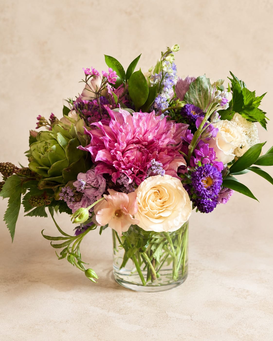 Mixed bouquet of pink, purple, and cream flowers in a clear glass vase
