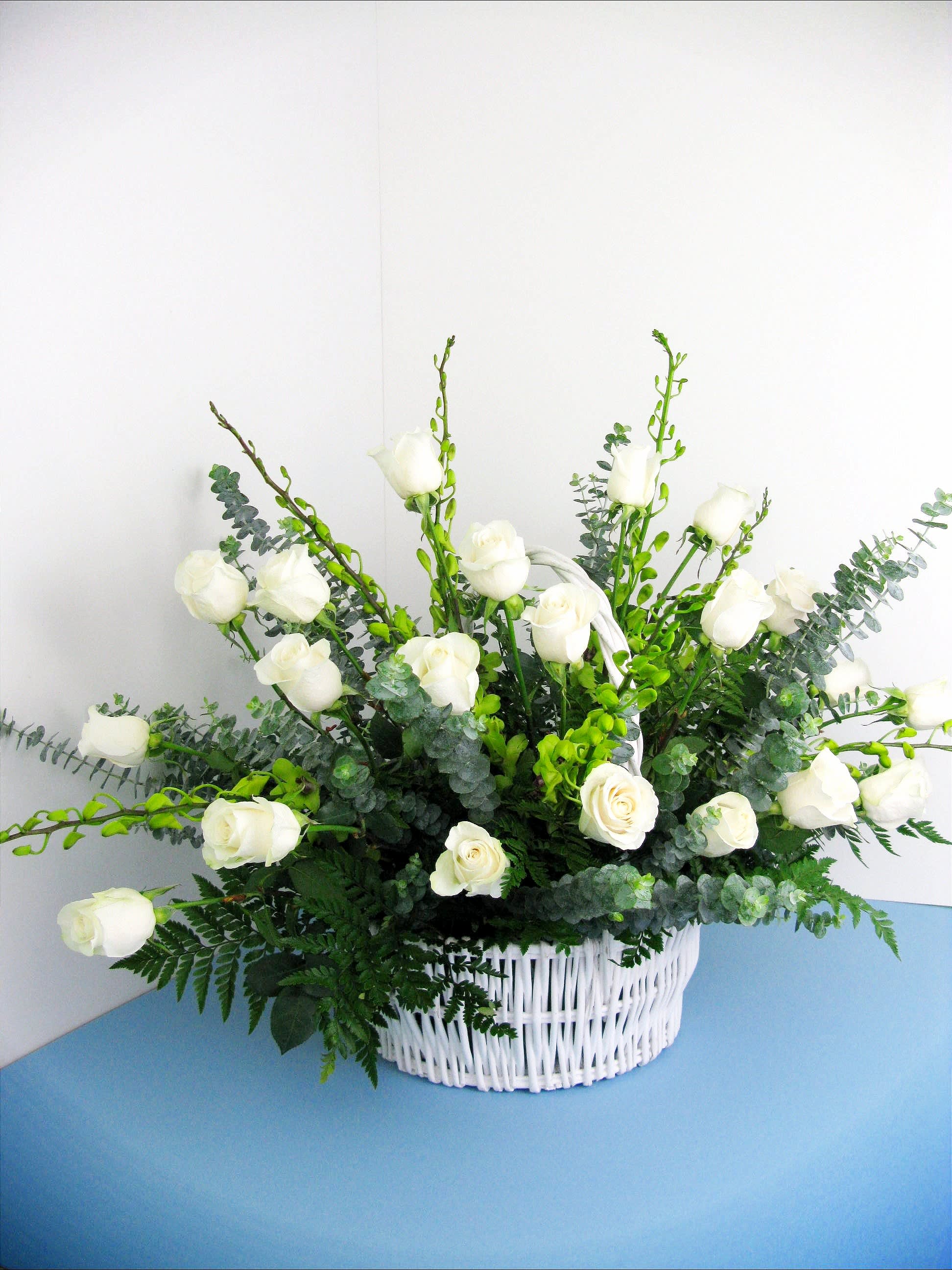 White roses arranged in a white wicker basket with greenery