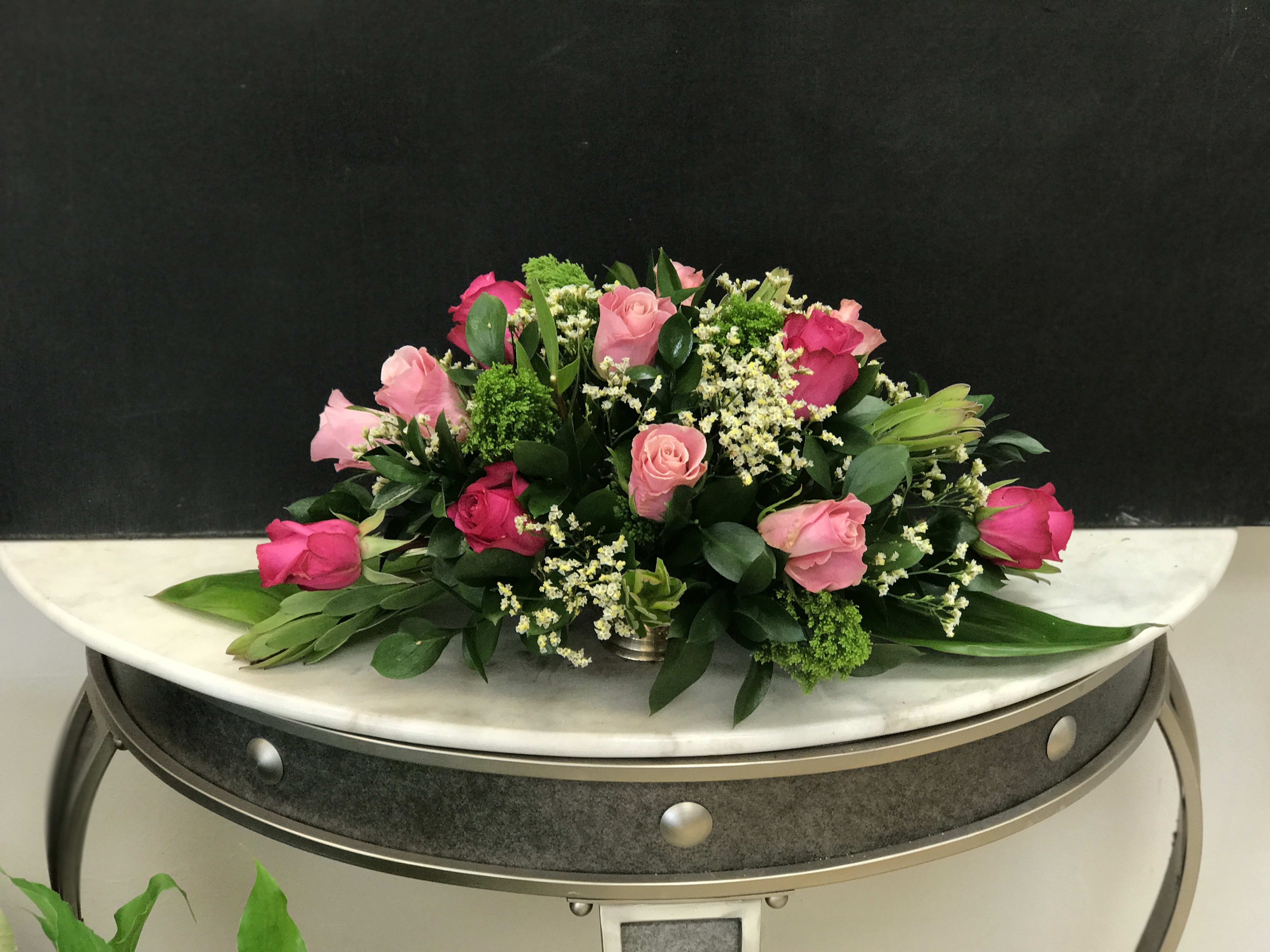Low arrangement of light and hot pink roses with white filler flowers in a silver container
