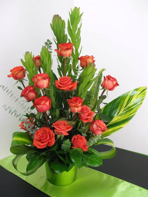 Arrangement of orange roses in a bright green pot with tall green accents and striped leaves