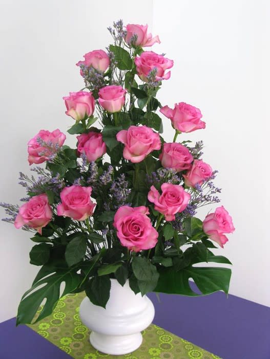 Tall arrangement of pink roses with purple filler flowers in a white vase