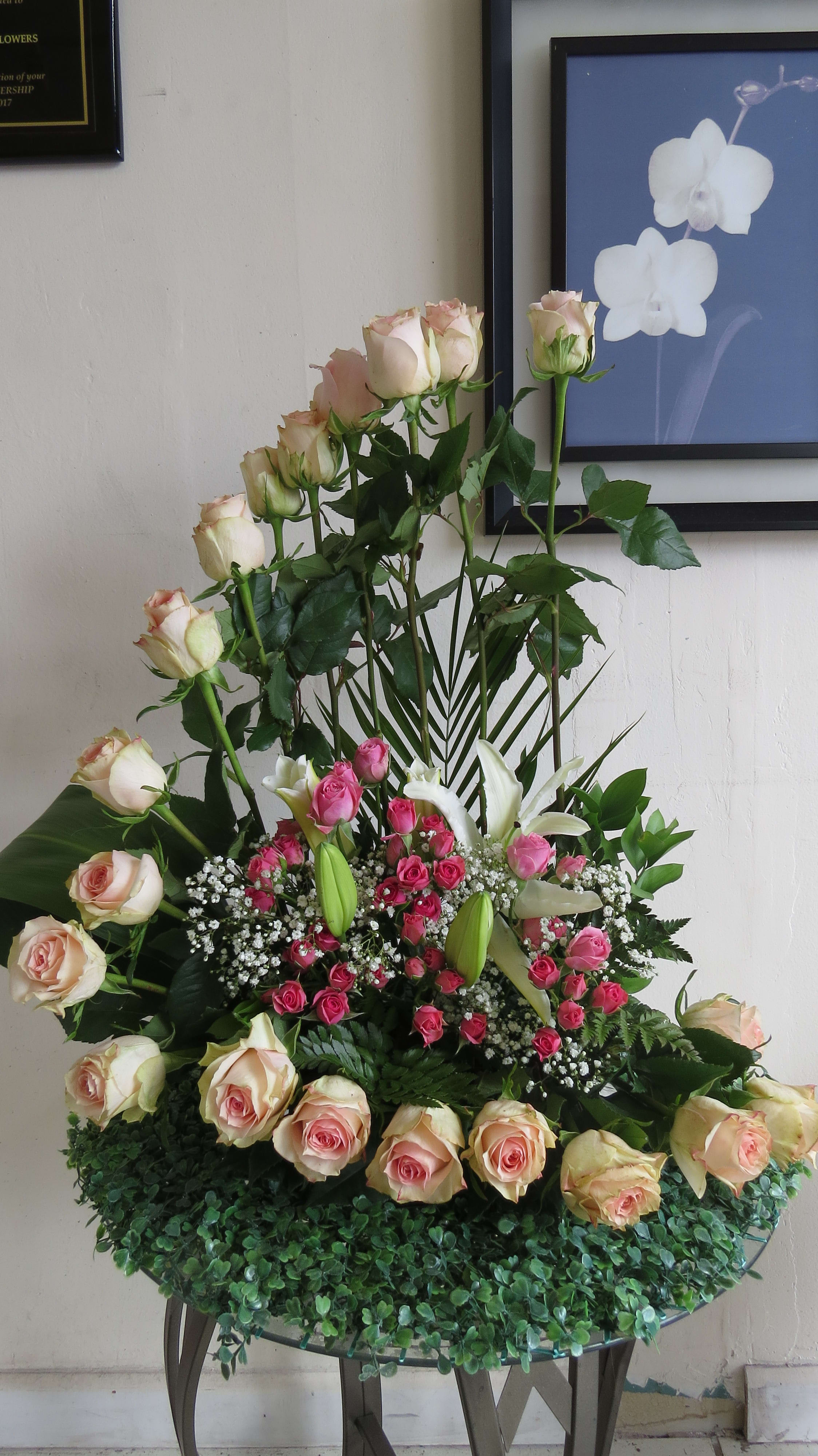 Tall arrangement of cream and pink roses with white lilies and small pink roses in a curved design