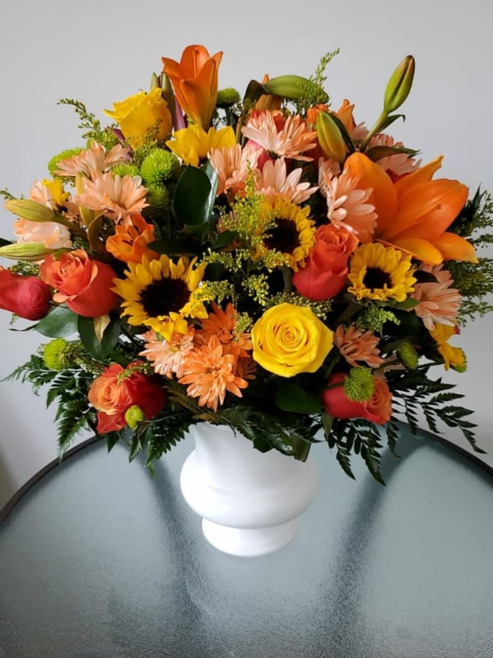 Mixed bouquet of orange, yellow, and pink flowers in a white vase
