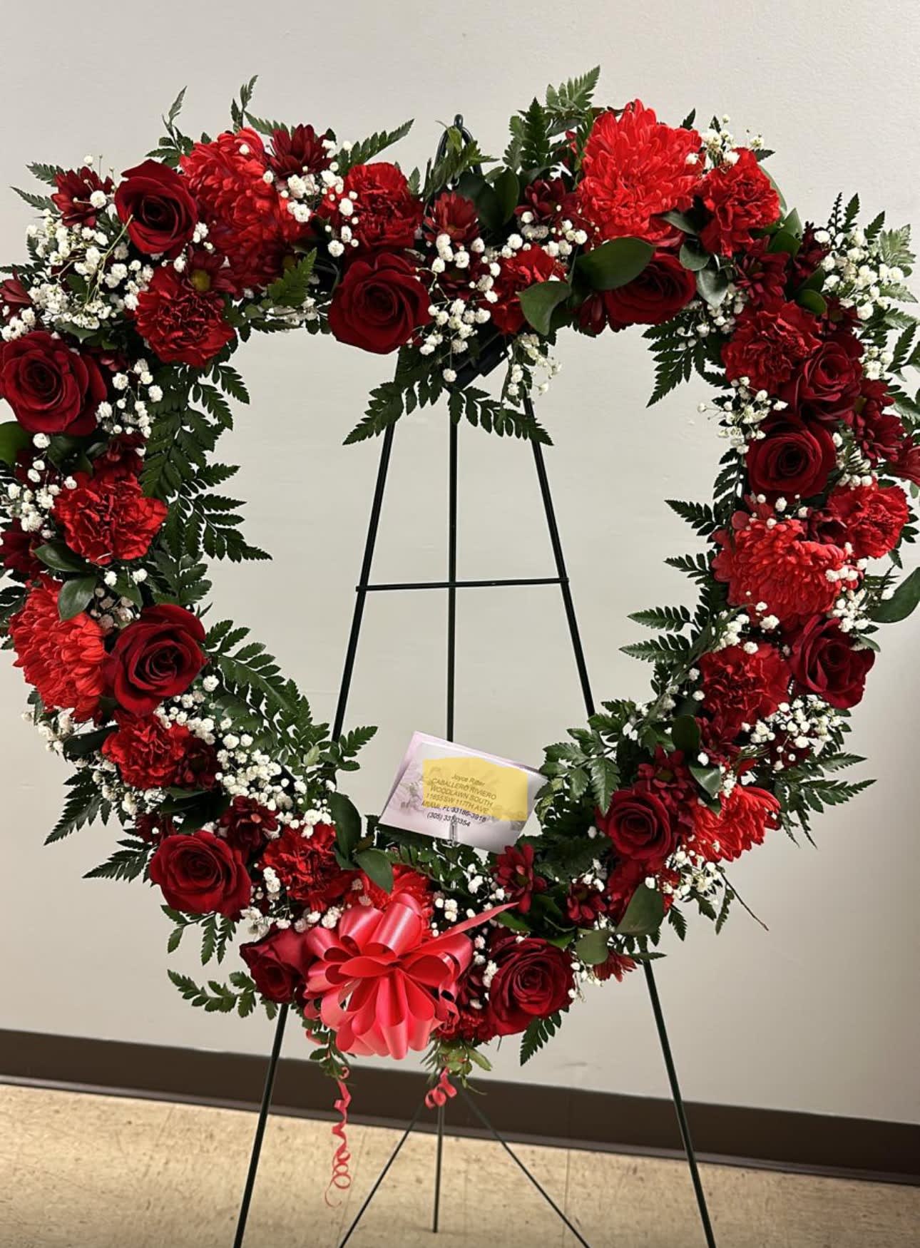Heart-shaped red floral wreath on an easel with a pink bow