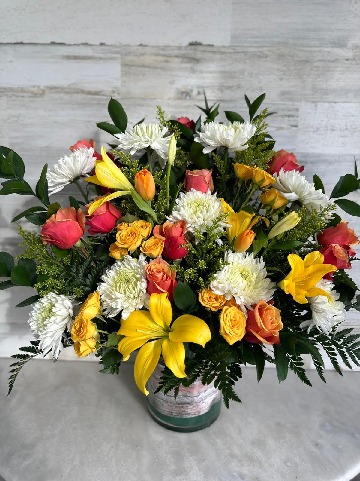 Mixed bouquet of yellow lilies, roses, and white chrysanthemums in a vase