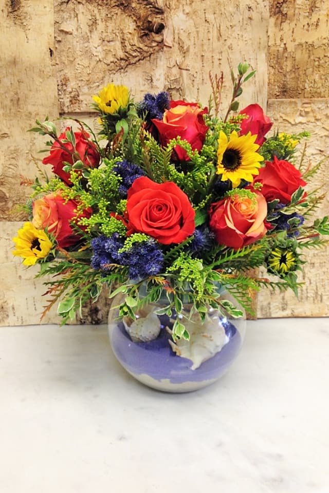 Mixed bouquet of red roses and yellow sunflowers in a round glass vase