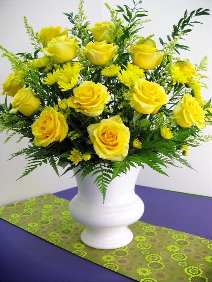 Arrangement of yellow roses and yellow daisies in a white urn vase on a purple table