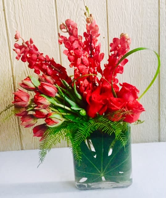 Red floral arrangement in a clear square vase with fern foliage