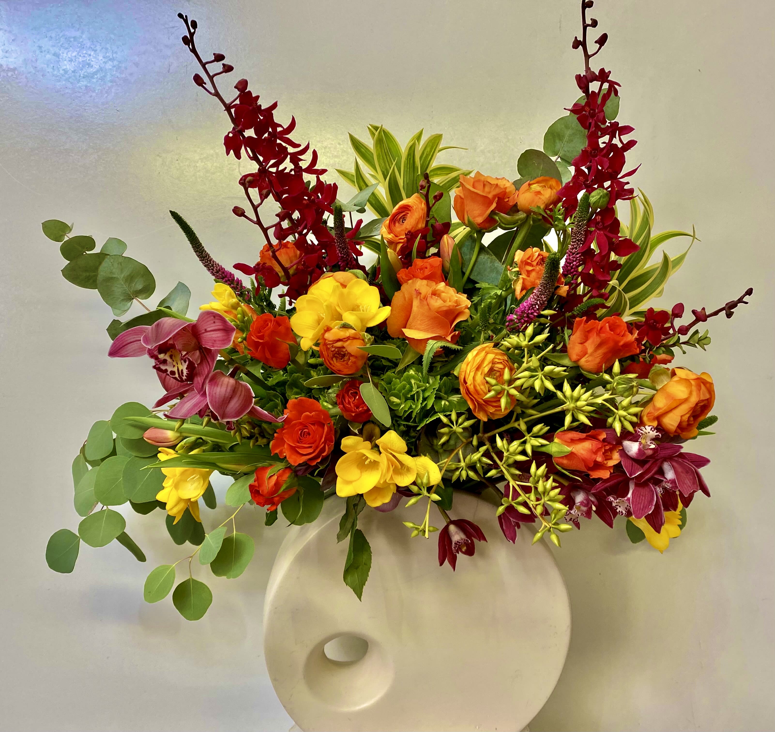 Bright mixed flower arrangement in a white vase with red, orange, yellow, and purple blooms.