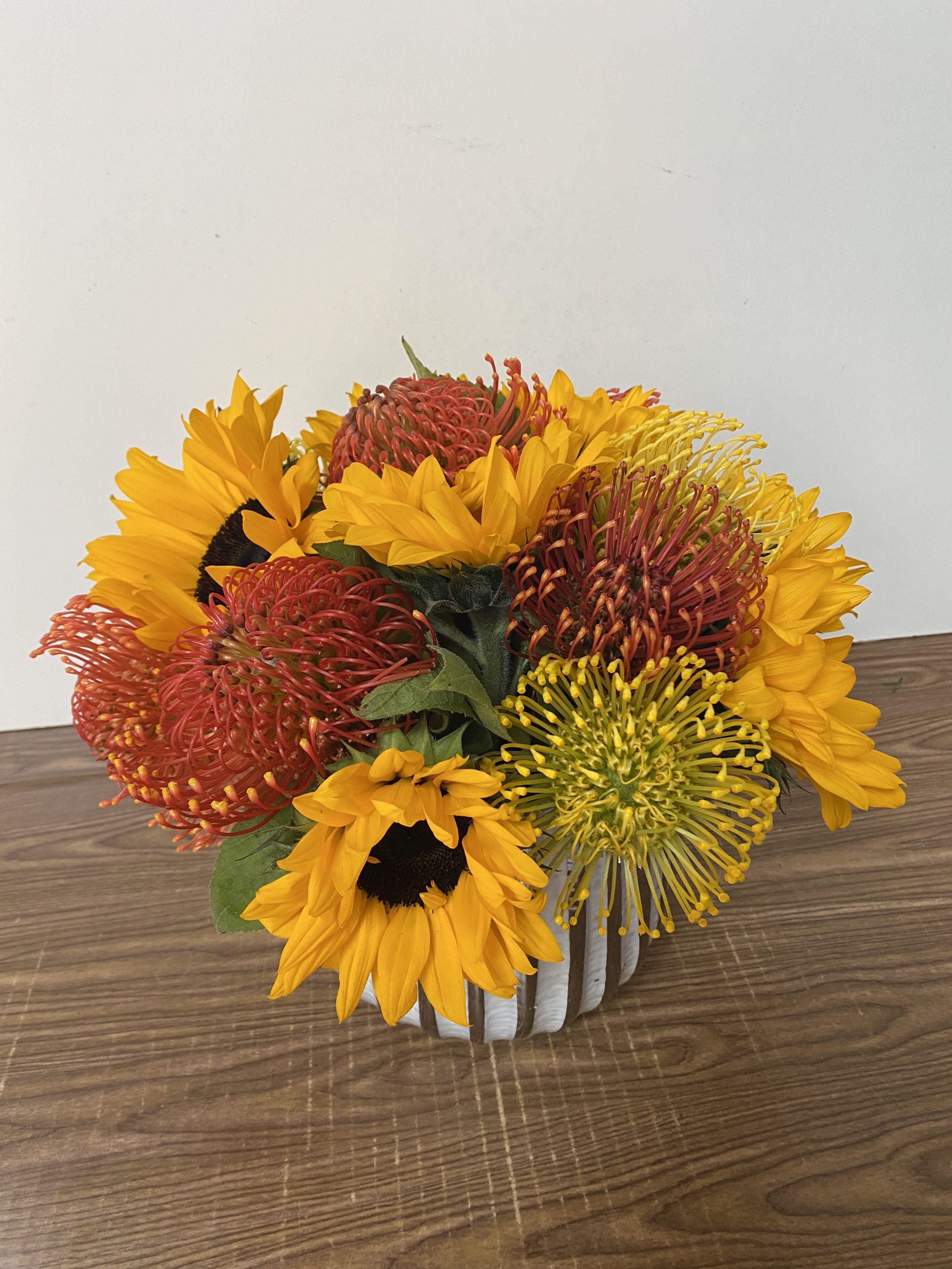Bouquet of sunflowers and red pincushion protea in a white container