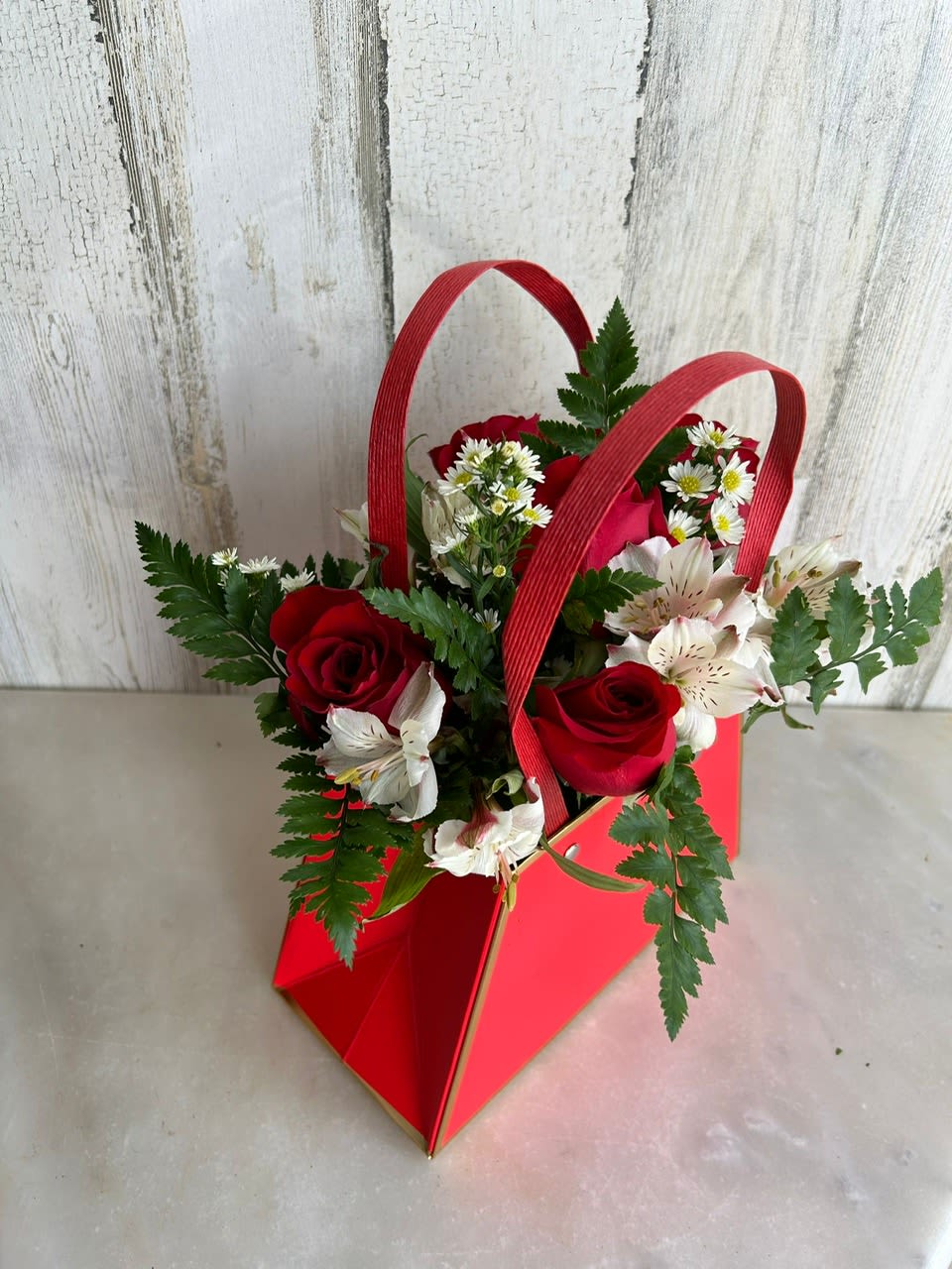 Red roses and white flowers in a red handled gift bag