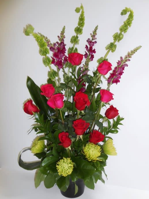 Tall bouquet of red and pink roses with green and purple spikes in a black vase