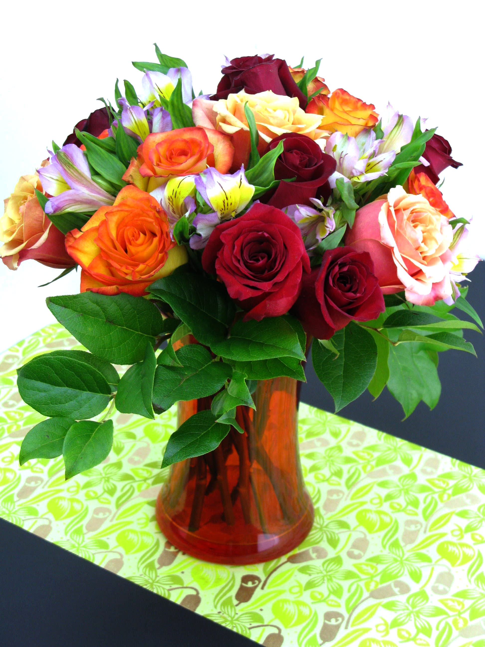 Bouquet of red, orange, and peach roses with alstroemeria in an orange glass vase