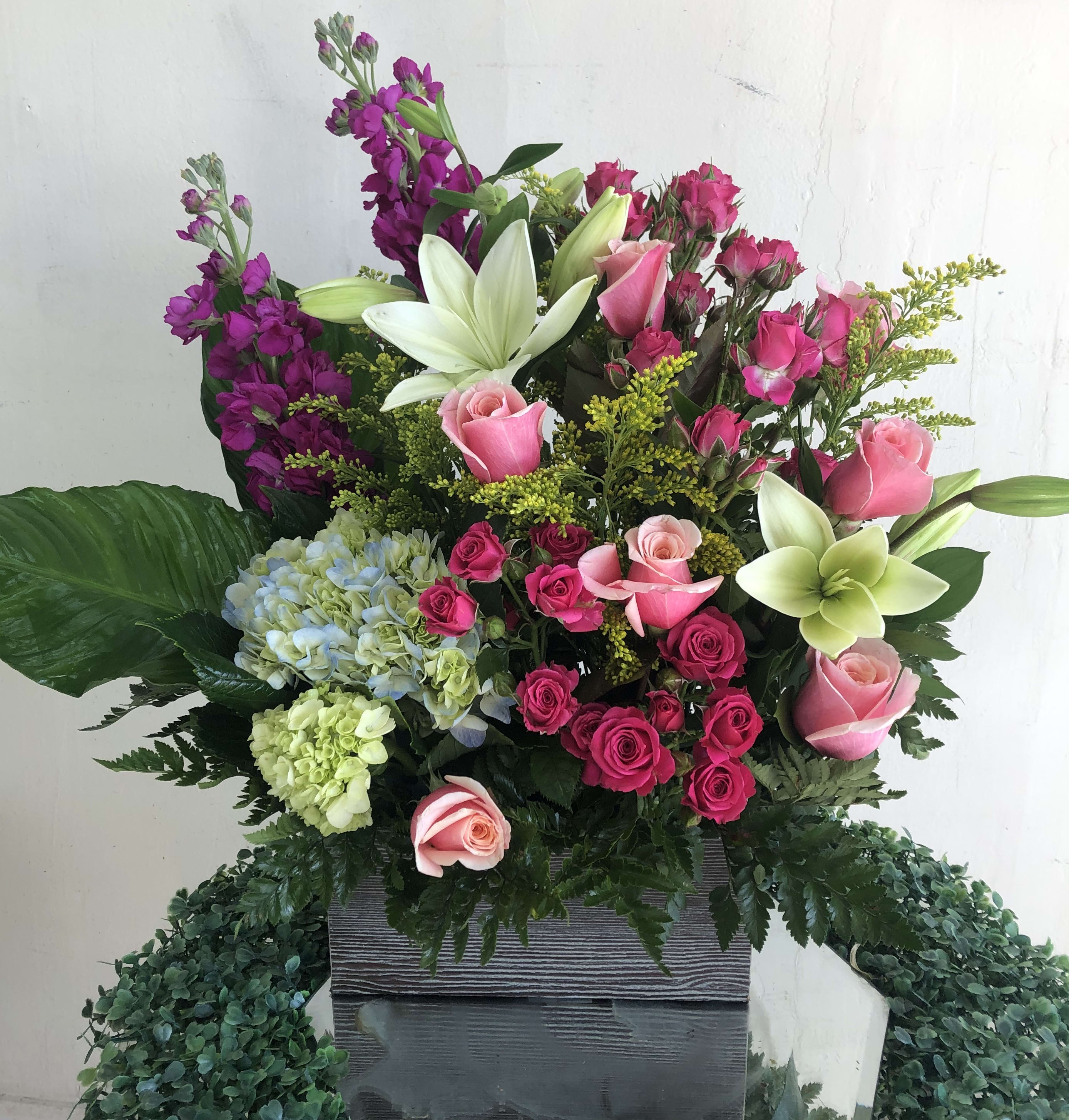 Tall arrangement of pink roses, white lilies, and hydrangeas in a rectangular gray container