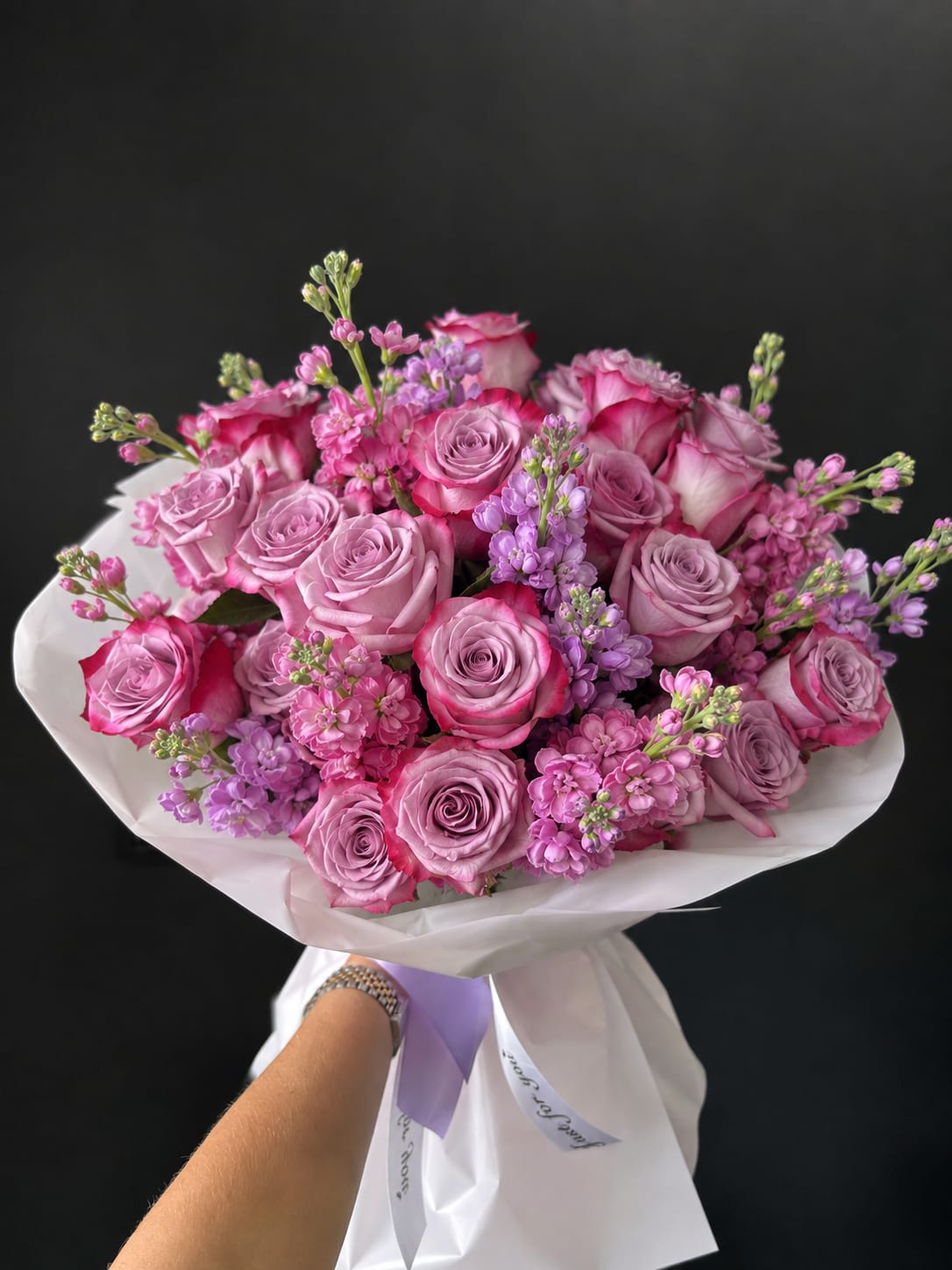 Hand-tied bouquet of pink and lavender roses with small purple filler flowers