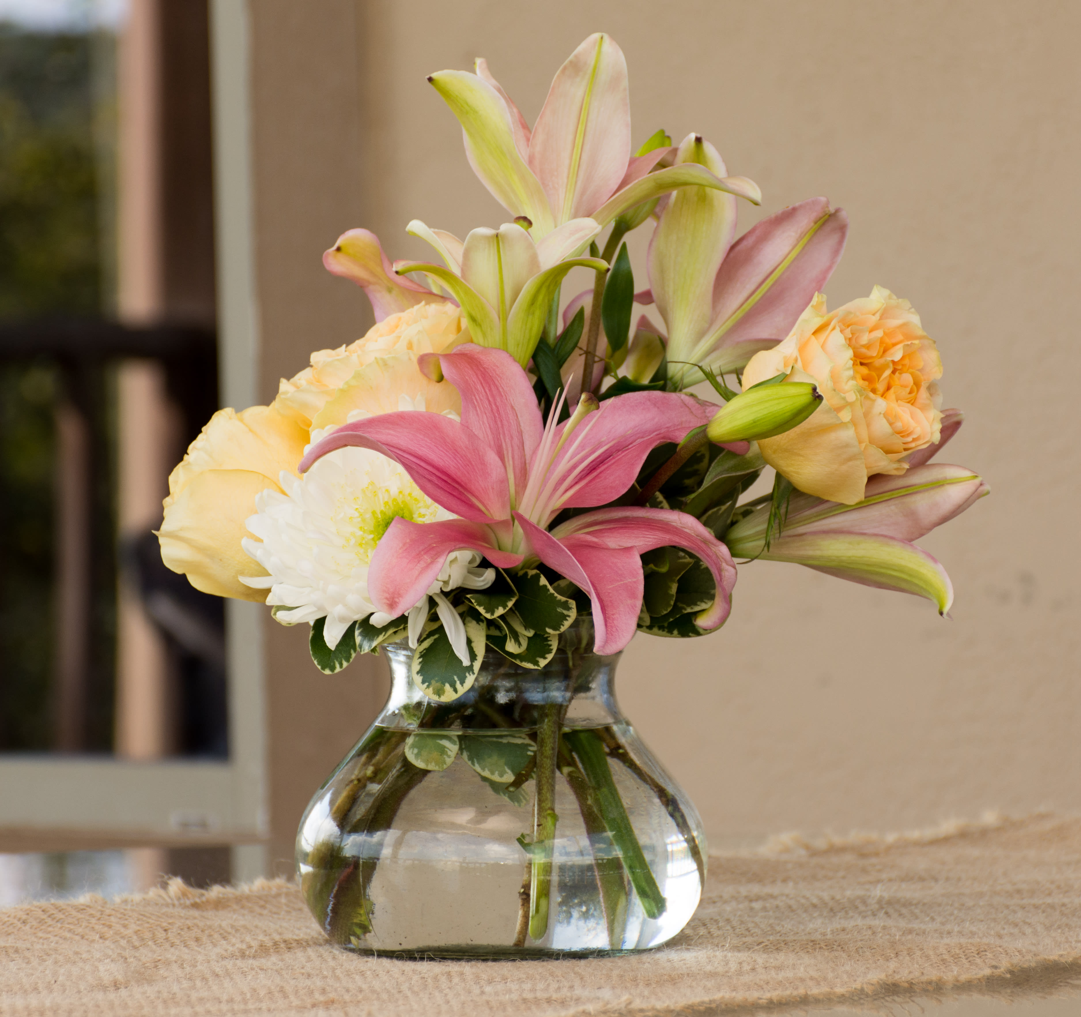 Pink lilies and pale roses arranged in a clear glass vase