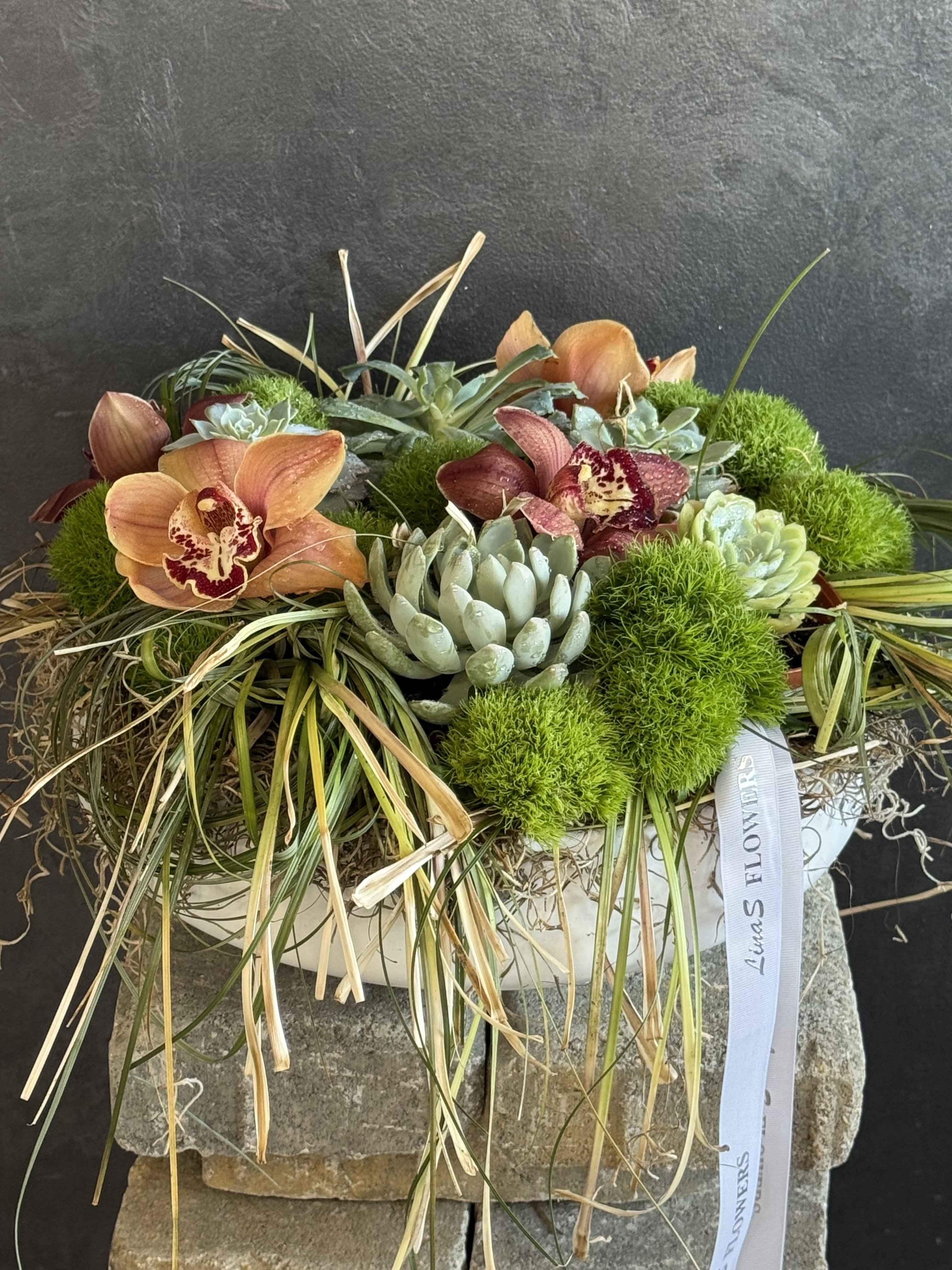 Orchid and succulent arrangement in a white container with trailing grass