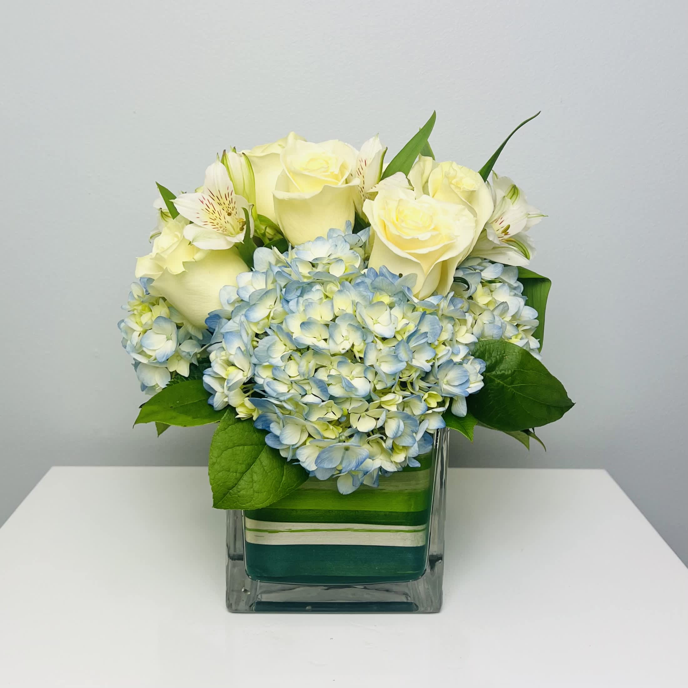 Cape Cod - Enjoy the seaside vibes of Cape Cod with this arrangement consisting of Blue Hydrangea, White Roses and Alstroemeria in a leaf wrapped Clear Glass Cube.  Approximately 10” Tall