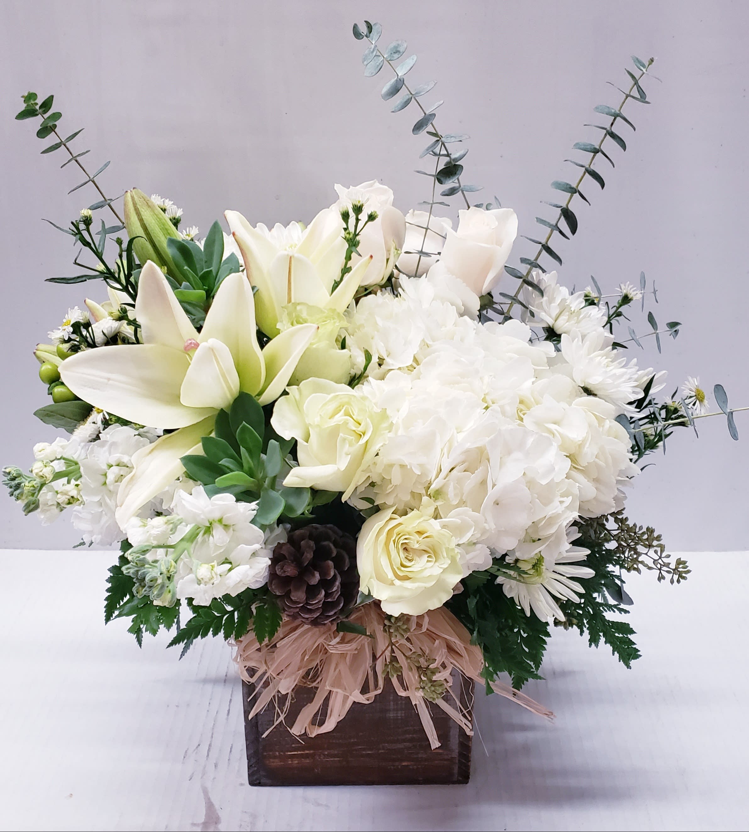 White floral arrangement with lilies, roses, and hydrangeas in a wooden box