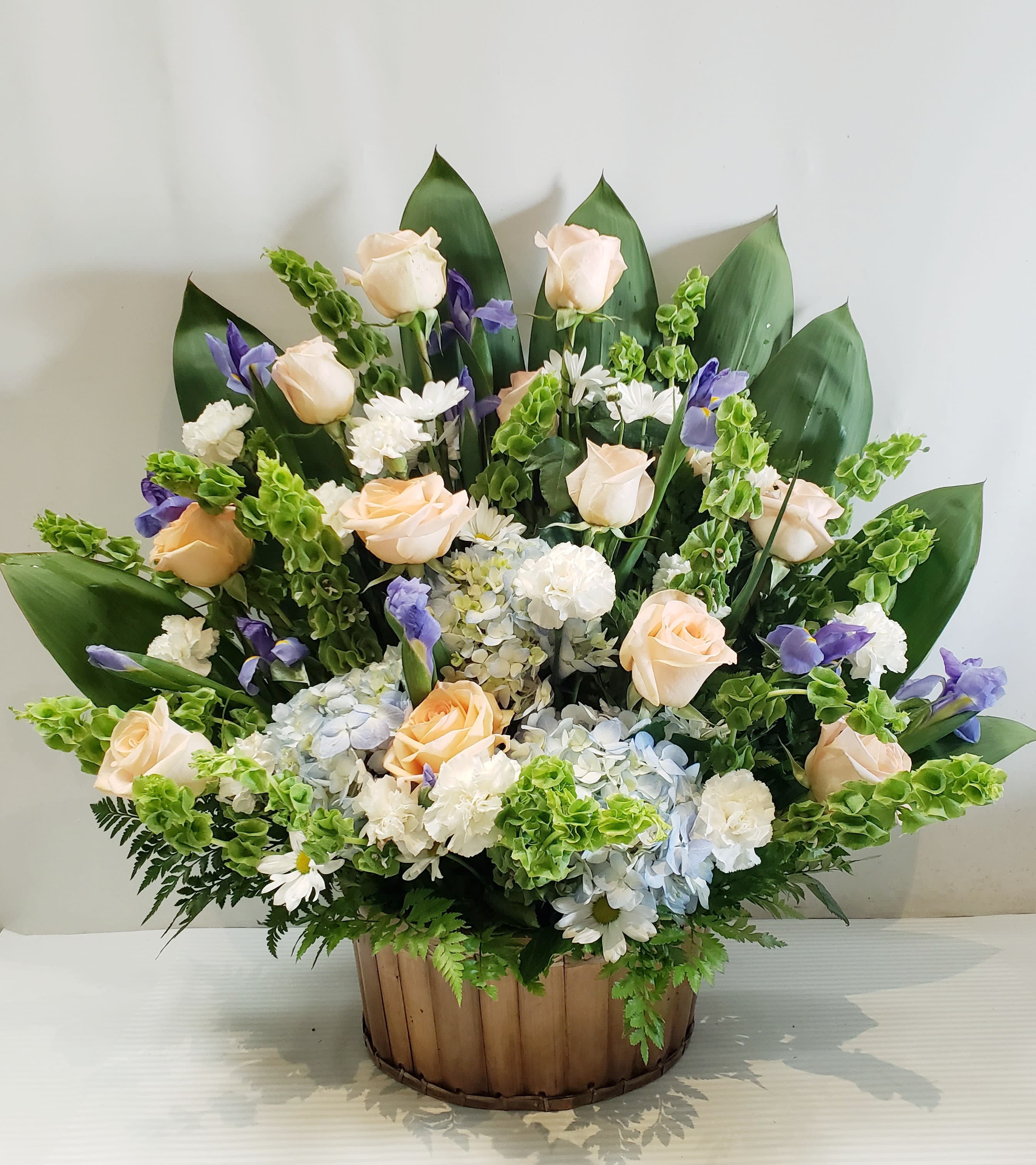 Arrangement of pale roses, white daisies, and purple flowers in a wooden basket