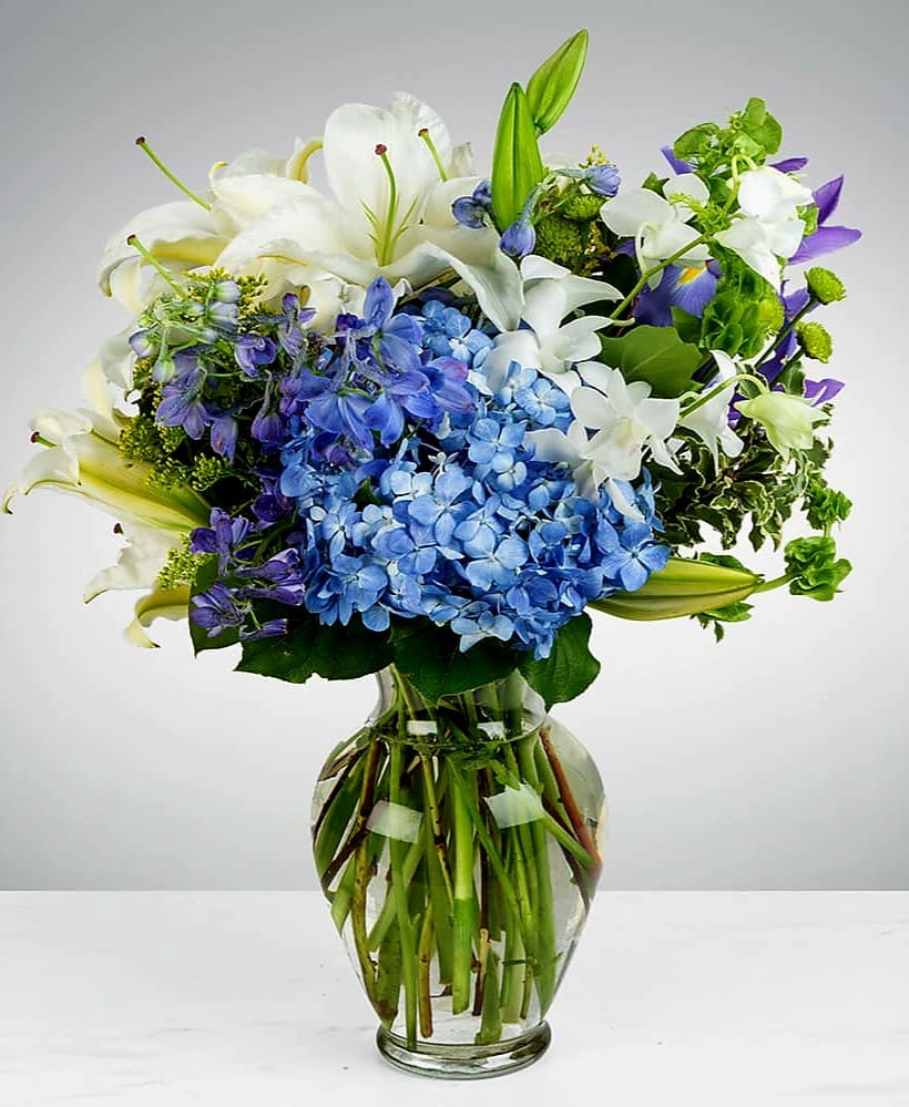 Blue hydrangeas and white lilies in a clear glass vase