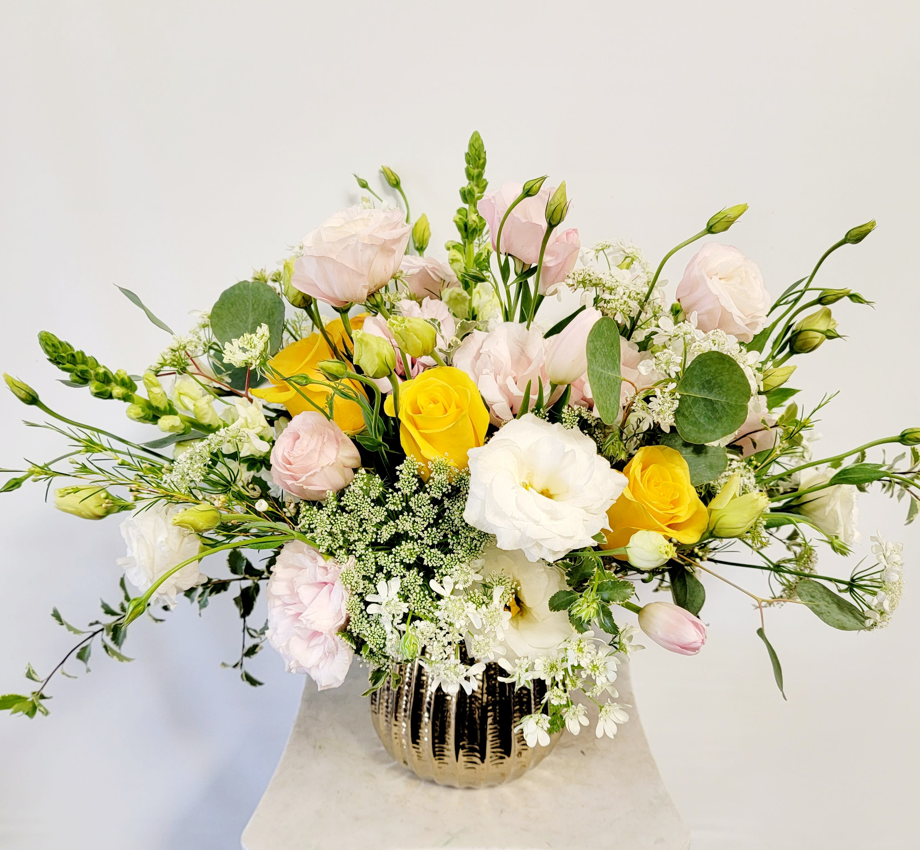 Mixed bouquet of yellow, white, and pale pink flowers in a gold vase