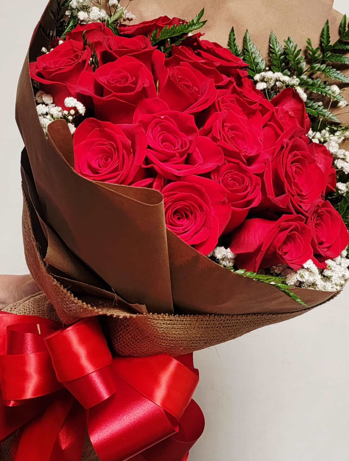 Large bouquet of red roses wrapped in brown paper with white filler flowers and a red ribbon bow.