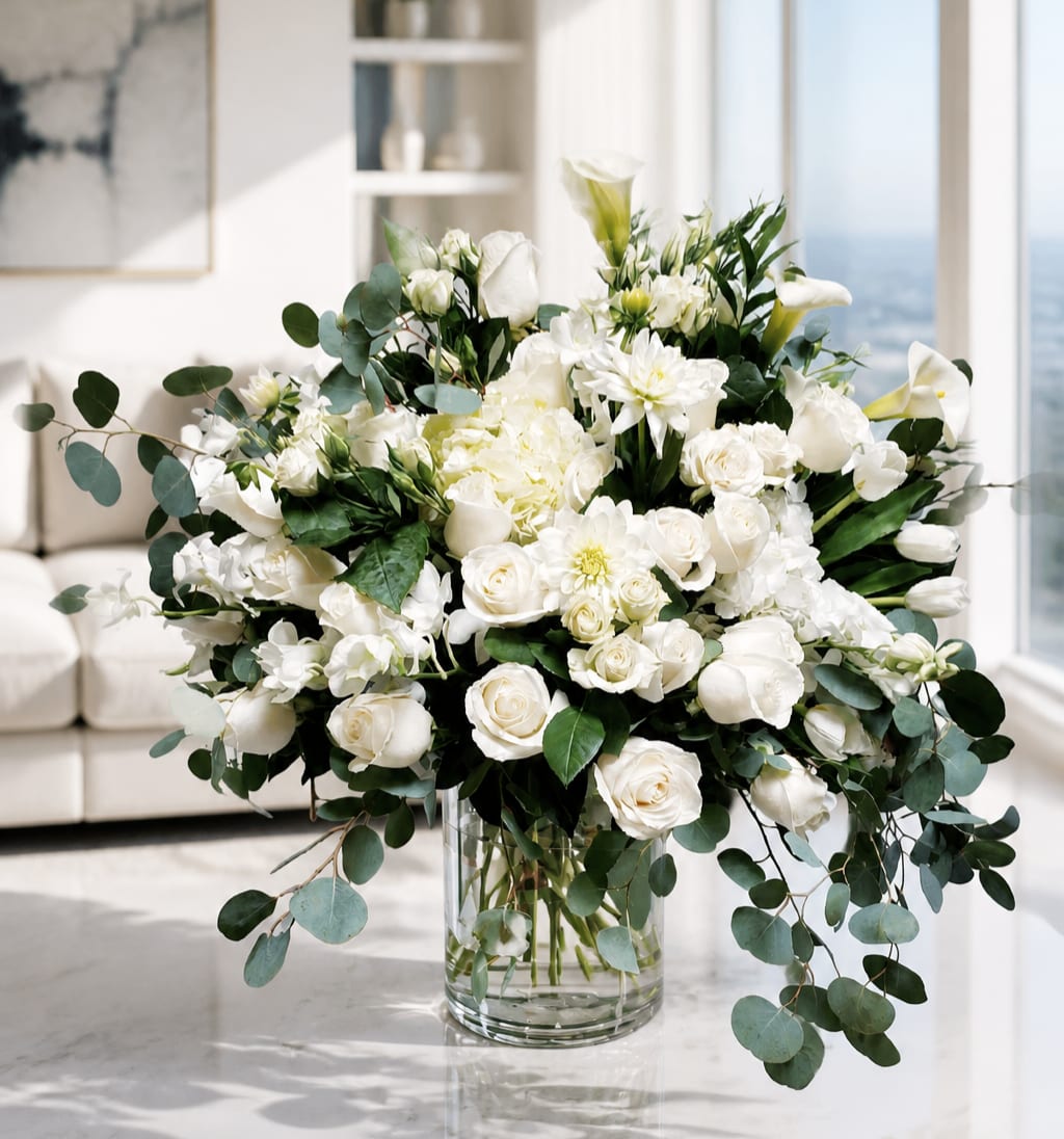 White floral arrangement in a clear glass vase with trailing eucalyptus