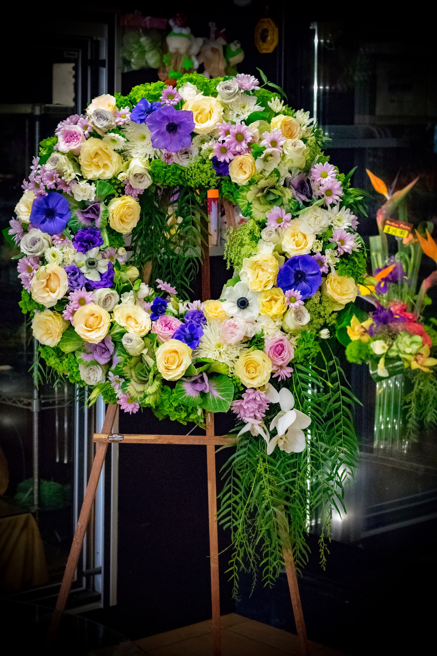 Large floral wreath on an easel with purple, yellow, white, and pink flowers