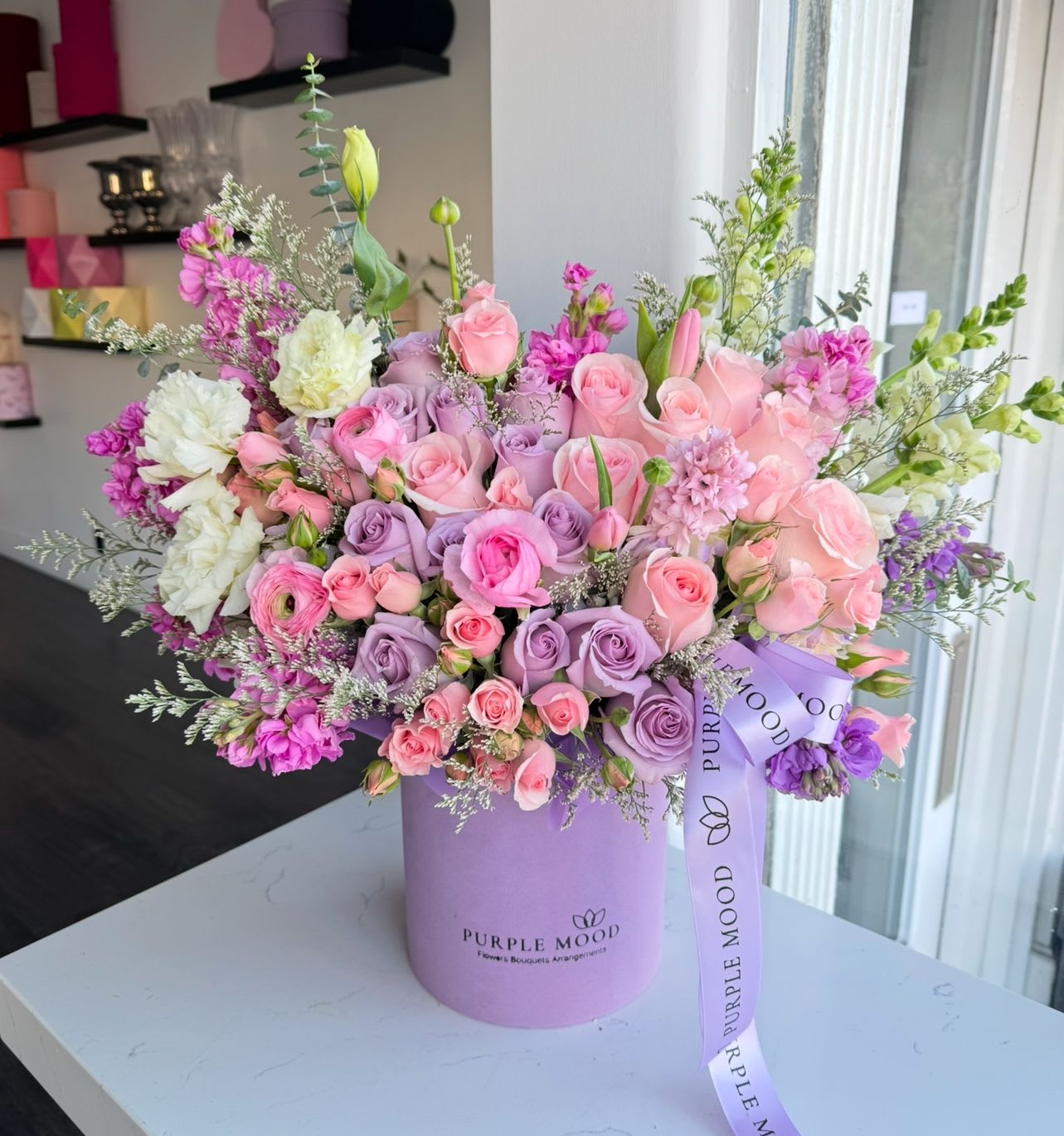 Lollipop Box - Standard container size - D6.75'x H7.5'  Deluxe container size - D8.25'x H9.5'  Premium container size - D10.5'x H12.25'  Playful, colorful, and full of sweetness — the Lollypop Box is a cheerful mix of pinks, lavenders, and purples, arranged in a stylish pastel box. Bright and vibrant, it’s the perfect choice to surprise someone special or add a pop of color to any celebration.  Key Features:     •    Styled in a pastel box with a bold, joyful design     •    Finished with a signature ribbon for a polished look     •    Available in Standard ($197), Deluxe ($264), Premium ($369) sizes     •    A fun and vibrant gift for birthdays, celebrations, or just because  Front side arrangement with a lid in the back. Box includes wet floral foam on the inside, box doesn't require vase.