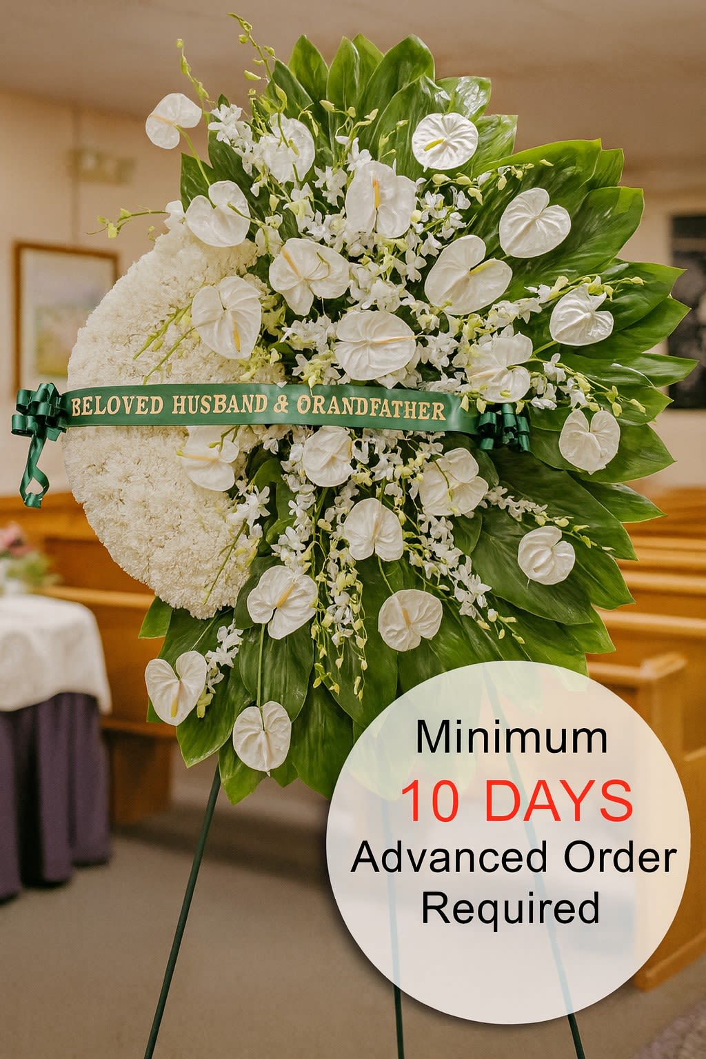 Tall white sympathy standing spray with clustered white flowers and glossy green leaves on an easel.