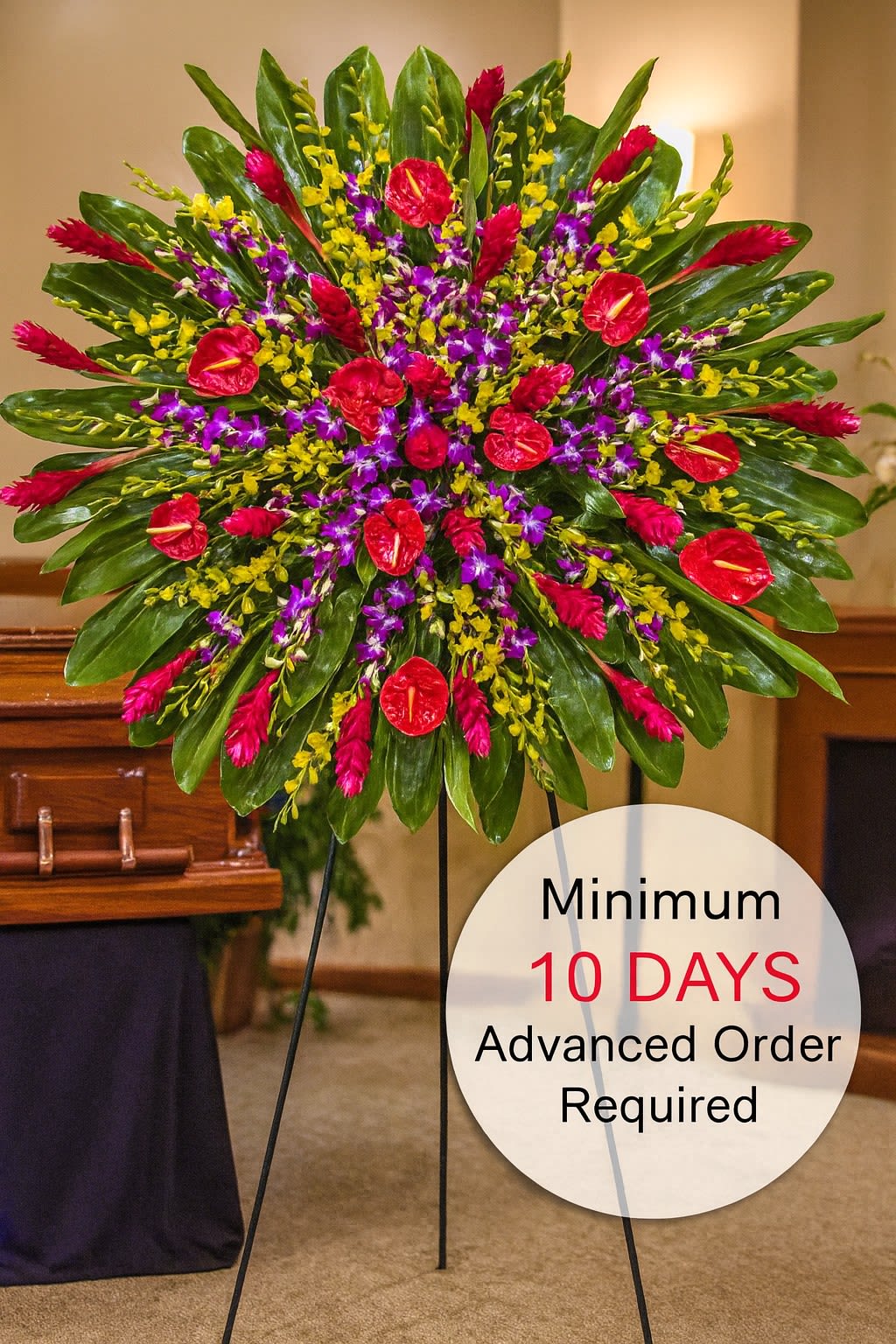 Large round tropical standing spray with red, purple, and yellow flowers on a metal easel in a funeral setting