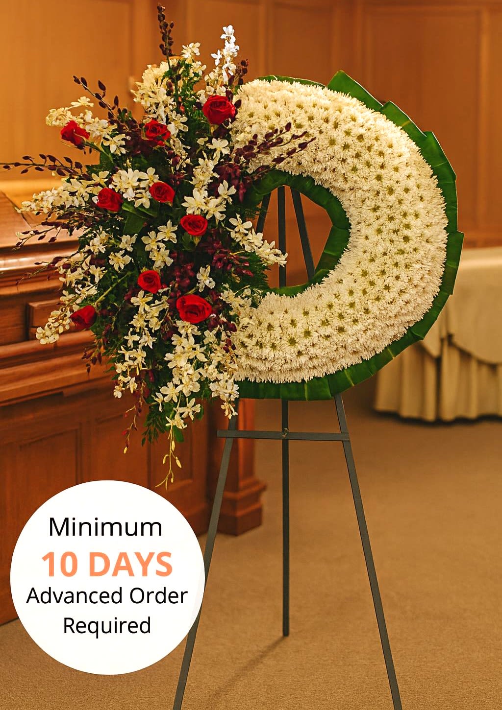 Large white crescent funeral wreath with red roses and white orchids on a metal easel stand.