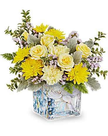 Compact arrangement of yellow and cream flowers in a square glass vase with a dove design