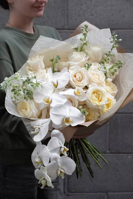 White roses and orchids in a hand-tied bouquet with cream wrapping