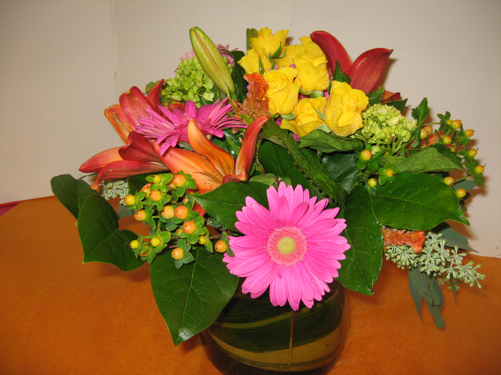 Mixed bouquet of yellow roses, pink gerbera daisies, and lilies in a glass vase