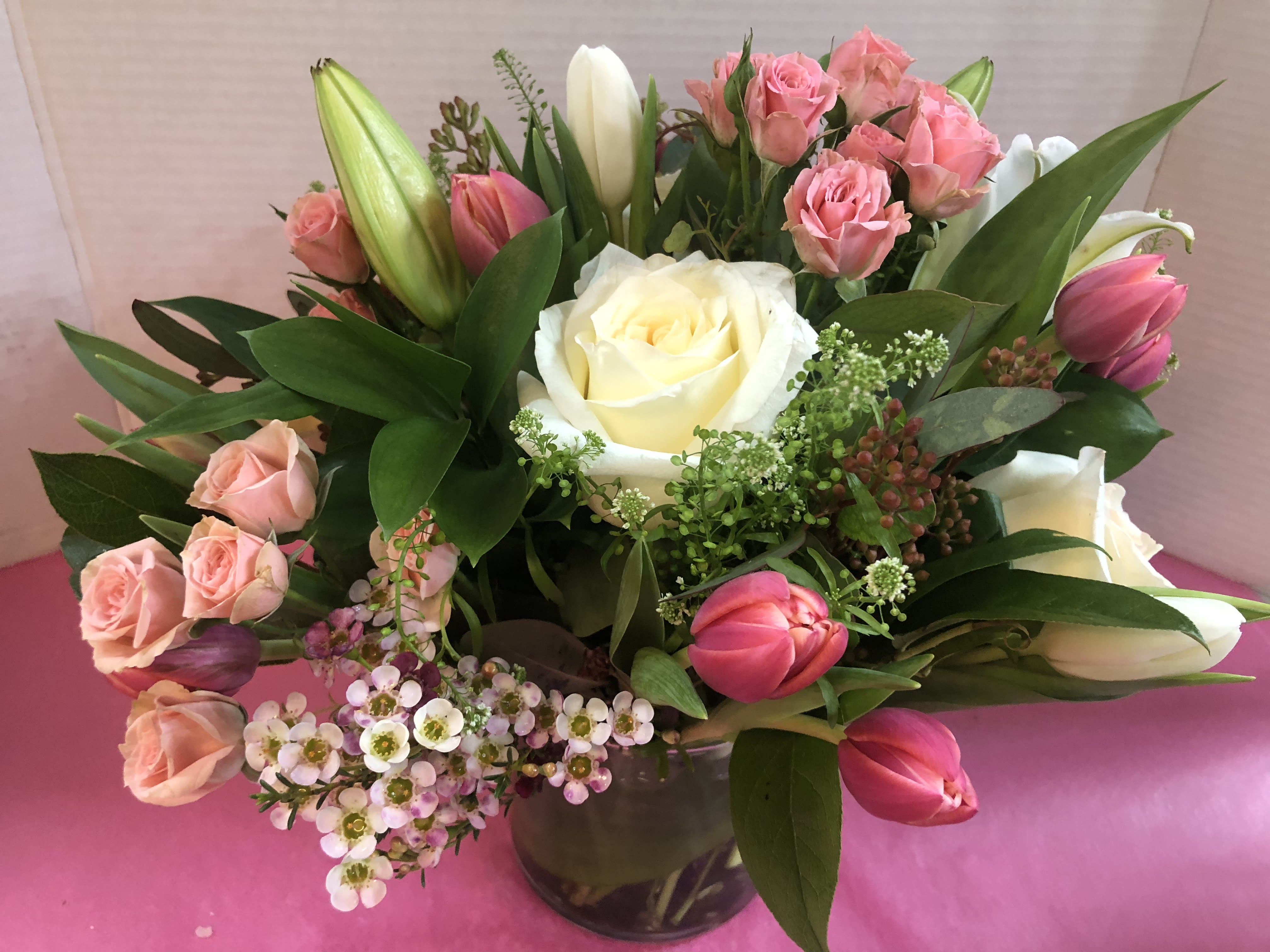 Compact arrangement of white roses, pink spray roses, and tulips in a clear glass vase
