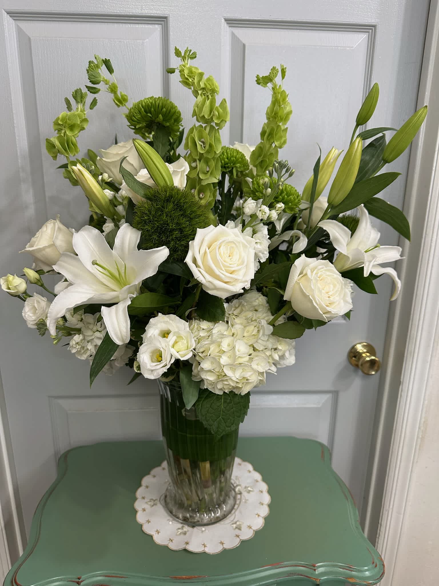 White lilies, roses, and green blooms arranged in a clear glass vase.